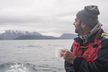 Älterer Mann schaut auf das Meer, Bootsfahrt auf dem Eyjafjordur Fjord, Island - UUF18800