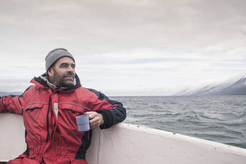 Mature man looking at the sea, boating on Eyjafjordur Fjord, Iceland - UUF18805