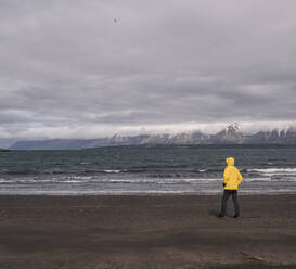 Matuer man standing on lava beach at Eyjafjordurfjord, Iceland, looking at the sea - UUF18809