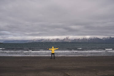 Matuer man standing on lava beach at Eyjafjordurfjord, Iceland, with arms out - UUF18810