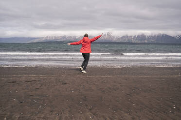 Young woman dancing on lava beach at Eyjafjordur fjord, Iceland - UUF18811