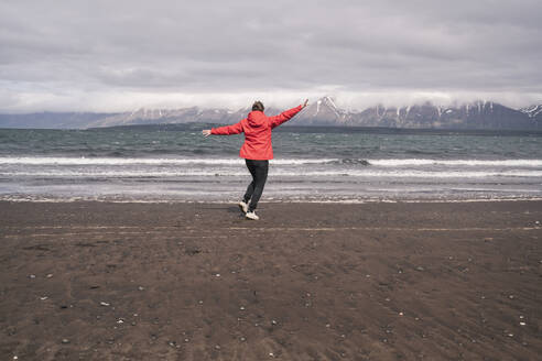 Junge Frau tanzt am Lavastrand am Eyjafjordur Fjord, Island - UUF18811