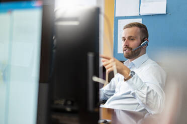 Geschäftsmann mit Headset am Schreibtisch im Büro - DIGF07944