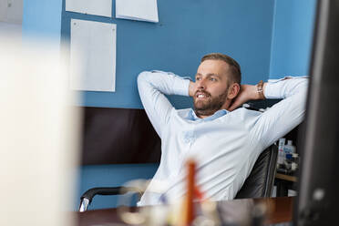 Smiling businessman leaning back at desk in office - DIGF07945