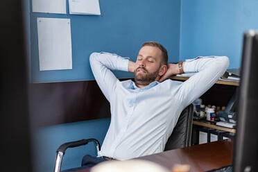 Tired businessman leaning back at desk in office - DIGF07946