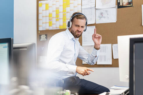 Geschäftsmann, der im Büro mit Kopfhörern Musik hört - DIGF07954