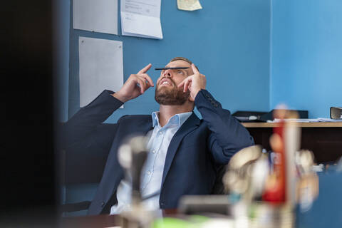 Geschäftsmann am Schreibtisch im Büro balanciert einen Stift auf seiner Nase, lizenzfreies Stockfoto