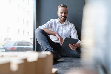 Glücklicher Geschäftsmann mit Tablet und Architekturmodell im Büro - DIGF07970