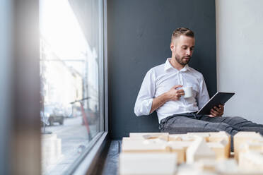 Geschäftsmann mit Tablet, Tasse Kaffee und Architekturmodell im Büro - DIGF07973