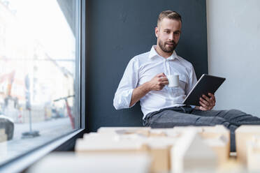 Geschäftsmann mit Tablet, Tasse Kaffee und Architekturmodell im Büro - DIGF07974