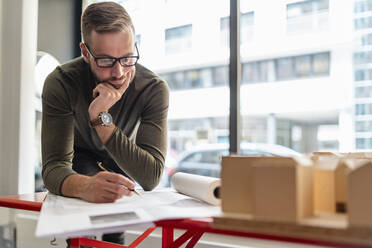 Mann arbeitet an einem Plan und einem Architekturmodell im Büro - DIGF07981