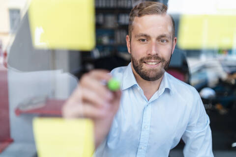 Businessman writing on adhesive notes at glass pane stock photo