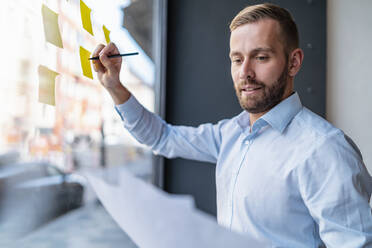 Businessman writing on adhesive notes at glass pane - DIGF07988