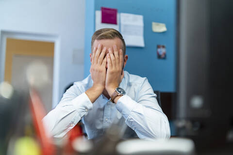 Geschäftsmann sitzt am Schreibtisch im Büro und hält die Hände vor das Gesicht, lizenzfreies Stockfoto