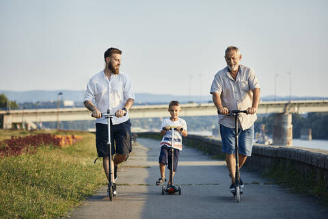 Grandfather, father and son riding scooters at the riverside stock photo