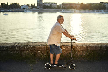 Älterer Mann fährt E-Roller am Flussufer - ZEDF02536