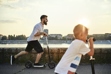 Vater und Sohn fahren Roller am Flussufer - ZEDF02537