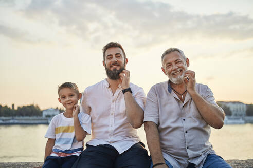 Portrait of smiling father and adult son with gandson scratching their beards - ZEDF02552