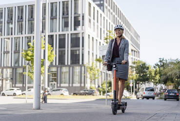 Happy businesswoman riding electric scooter on the street - DIGF08006