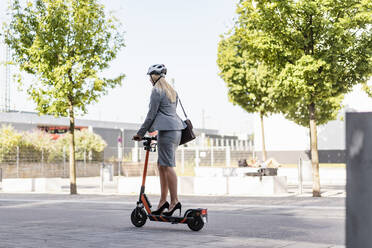 Businesswoman wearing high heels riding electric scooter on the street - DIGF08009