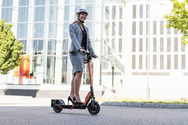 Businesswoman wearing high heels riding electric scooter on the street - DIGF08010