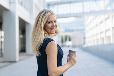 Portrait of smiling blond businesswoman with coffee to go in summer - DIGF08015