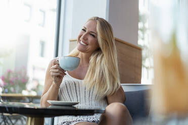 Porträt einer glücklichen blonden Frau beim Kaffeetrinken in einem Café - DIGF08018