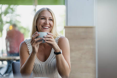 Porträt einer glücklichen blonden Frau beim Kaffeetrinken in einem Café, lizenzfreies Stockfoto