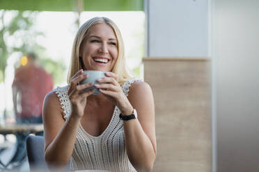 Portrait of happy blond woman drinking coffee in a cafe - DIGF08020