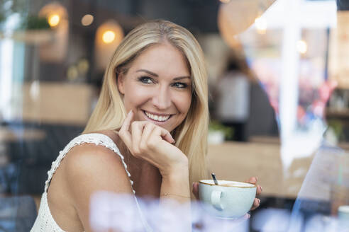 Porträt einer lächelnden blonden Frau, die in einem Café Kaffee trinkt - DIGF08022