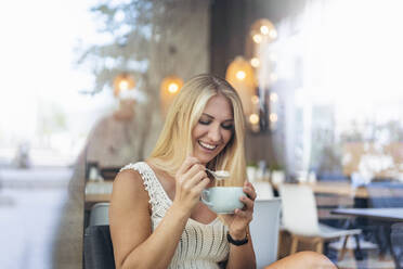 Porträt einer glücklichen blonden Frau, die in einem Cafe Cappuccino trinkt - DIGF08023