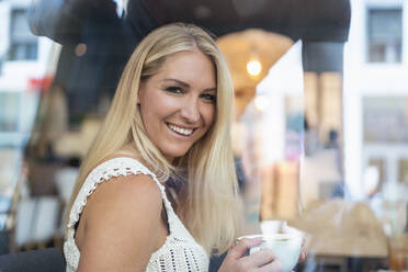 Porträt einer lächelnden blonden Frau, die in einem Café Kaffee trinkt - DIGF08024