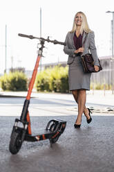 Portrait of happy businesswoman with electric scooter - DIGF08030