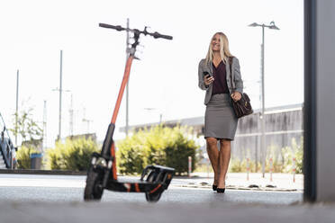 Portrait of happy businesswoman borrowing rental electric scooter - DIGF08031