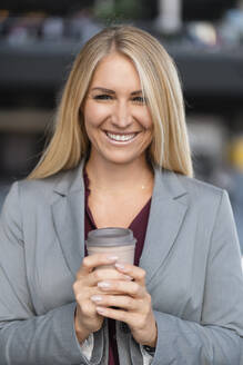 Porträt einer lächelnden blonden Geschäftsfrau mit Kaffee zum Mitnehmen - DIGF08037