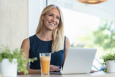 Porträt einer lächelnden blonden Geschäftsfrau mit Laptop in einem Kaffeehaus - DIGF08053