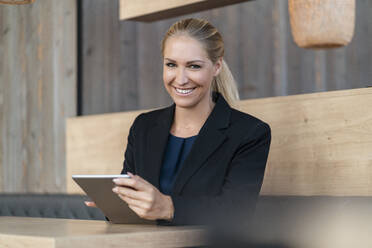 Porträt einer lächelnden blonden Geschäftsfrau mit digitalem Tablet in einem Café - DIGF08055