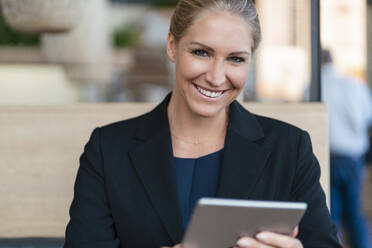 Portrait of smiling blond businesswoman with digital tablet in a coffee shop - DIGF08057