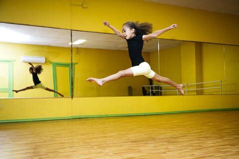 Gemischtrassiges Mädchen springt im Ballettstudio, lizenzfreies Stockfoto