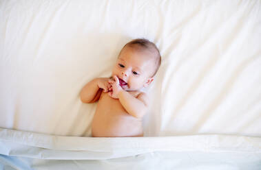 Portrait of baby boy lying on white bed sheet - OCMF00572