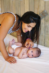 Happy mother playing with baby boy lying on bed - OCMF00573