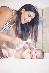 Happy mother playing with baby boy lying on bed - OCMF00575