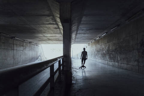 Silhouette eines jungen Mannes beim Longboarden in einem Tunnel, lizenzfreies Stockfoto