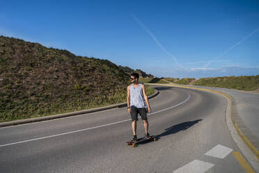 Young man longboarding on empty country road - AFVF03792