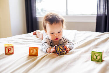 Kaukasisches Babymädchen spielt mit Blöcken auf dem Bett - BLEF14341