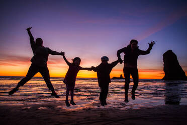 Silhouette einer vor Freude springenden kaukasischen Familie am Cannon Beach, Oregon, Vereinigte Staaten - BLEF14357