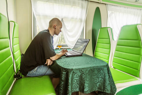 Kaukasischer Mann mit Laptop in grüner Kabine im Zug - BLEF14361