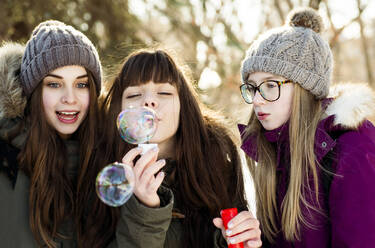 Caucasian girls blowing bubbles outdoors in winter - BLEF14367