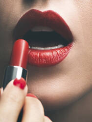 Nahaufnahme einer Frau, die roten Lippenstift aufträgt - BLEF14409