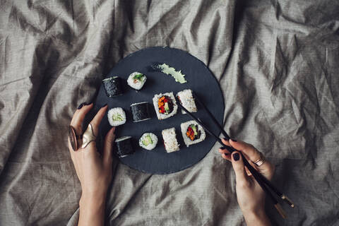 Hände einer Frau greifen nach einer Sushi-Platte auf dem Bett, lizenzfreies Stockfoto